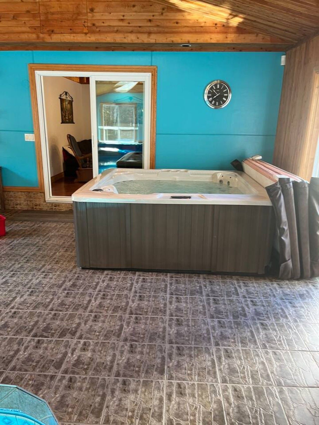 A hot tub in a room with a blue wall and wooden ceiling.