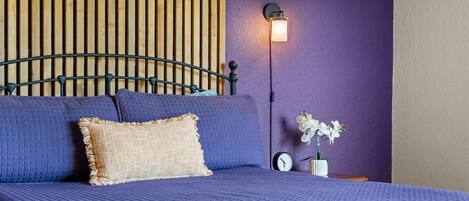 A bed with a headboard, a wall-mounted light, a clock, and a vase with flowers.