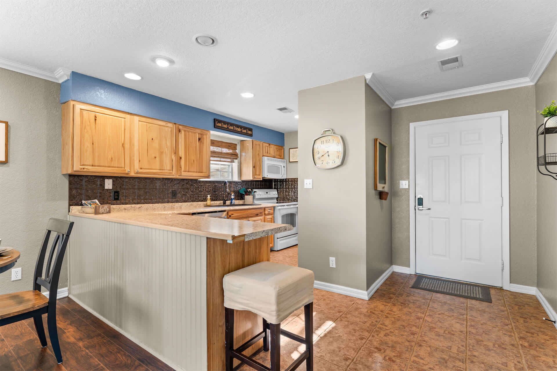 A kitchen with wooden cabinets, a central island, a microwave, and a clock on the wall.