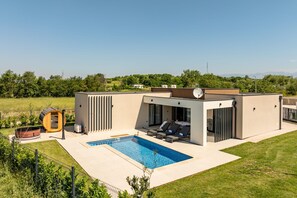 Ein moderner Poolbereich im Freien mit Whirlpool, Liegestühlen und einer überdachten Sitzgelegenheit.