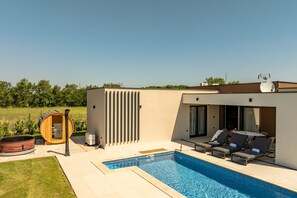 Ein moderner Poolbereich im Freien mit Liegestühlen, einem Whirlpool und einer überdachten Sitzgelegenheit.