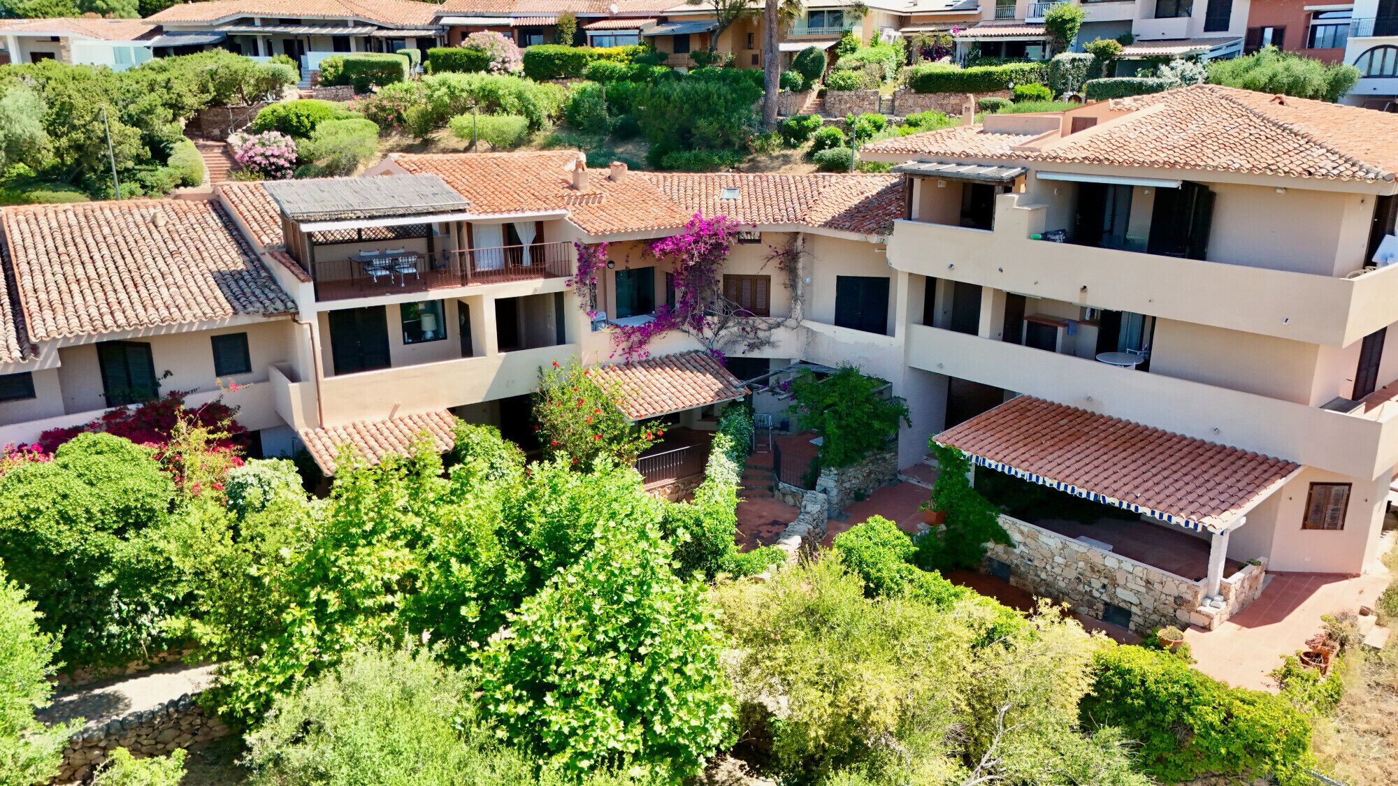 A residential complex with multiple two-story buildings, each featuring a tiled roof, balconies, and a courtyard with greenery.