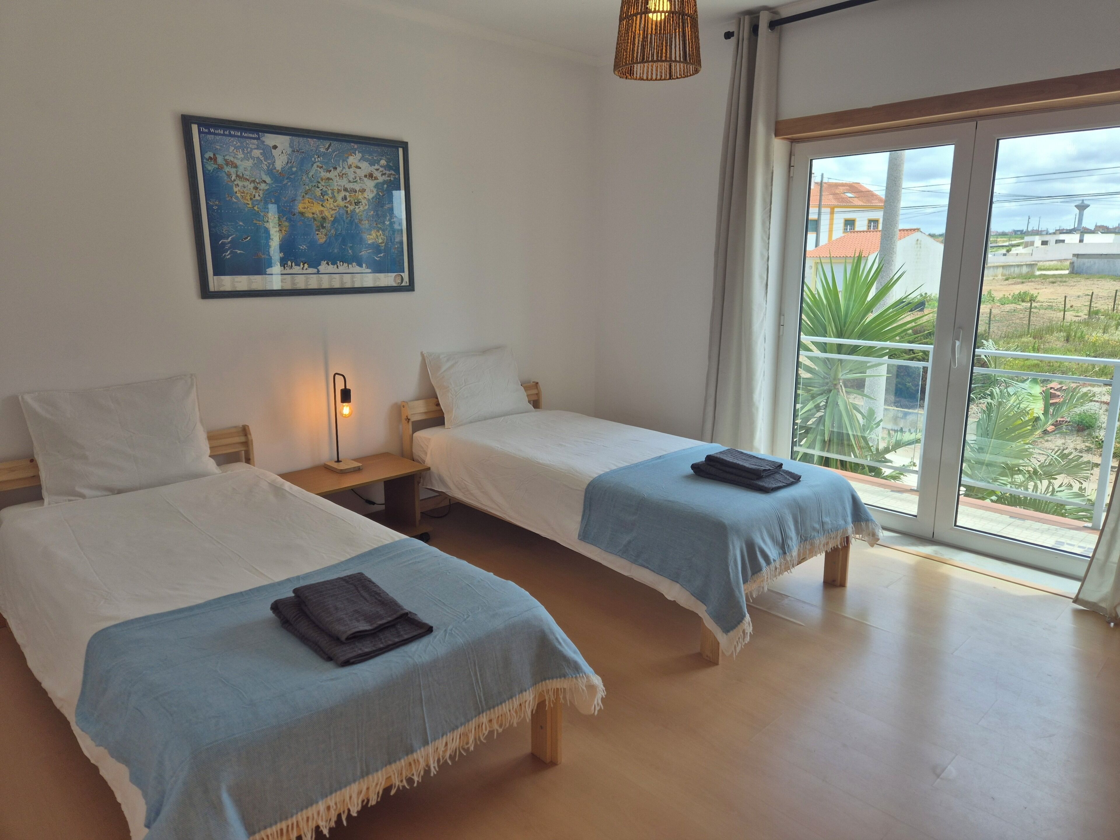 A hotel room with two beds, a map on the wall, a bedside lamp, and a view of the outside.