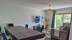 Ein modernes Wohnzimmer mit einem Holzesstisch, weißen Stühlen, einer Couch und einem an der Wand befestigten Fernseher.