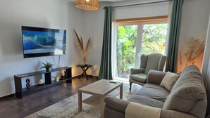 Ein modernes Wohnzimmer mit Sofa, Couchtisch, Fernseher und Blick auf Grün durch das Fenster.