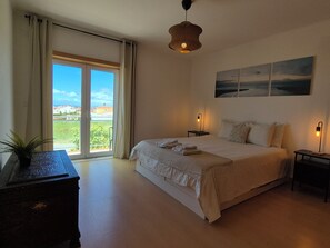 Ein Schlafzimmer mit einem großen Bett, zwei Nachttischen, einer Pendelleuchte, einem Fenster mit Vorhängen und Blick ins Freie.
