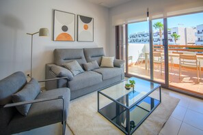Ein modernes Wohnzimmer mit grauem Sofa, einem Glastisch und einer Stehlampe.