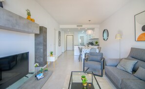 Ein modernes Wohnzimmer mit Flachbildfernseher, Glastisch und grauem Sofa.