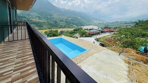 Ein Balkon mit Blick auf eine gebirgige Landschaft, ein Schwimmbad und ein kleines Gebäude mit rotem Dach.