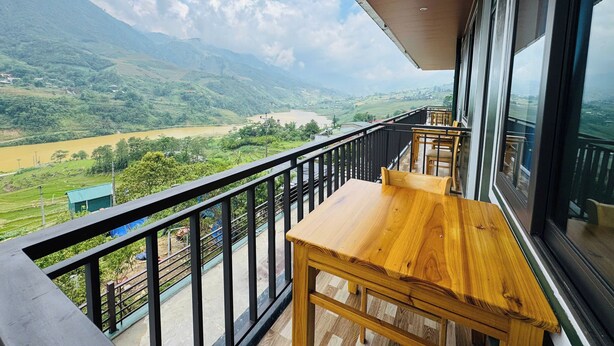Ein Balkon mit Holztisch und -stühlen, mit Blick auf einen Fluss und Berge.