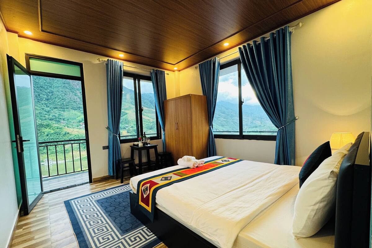 Un dormitorio con cama, armario de madera, mesa y sillas, y vistas al exterior.