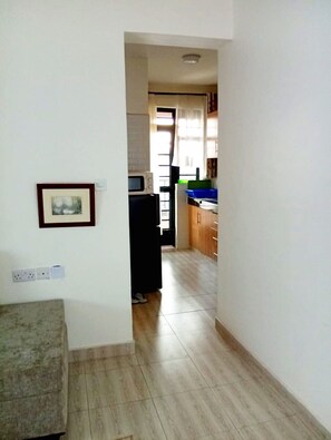 A narrow hallway leading to a kitchen with a microwave, cabinets, and a window with curtains. - Cozy 1 Bedroom apartment near JKIA and the SGR (Nairobi)