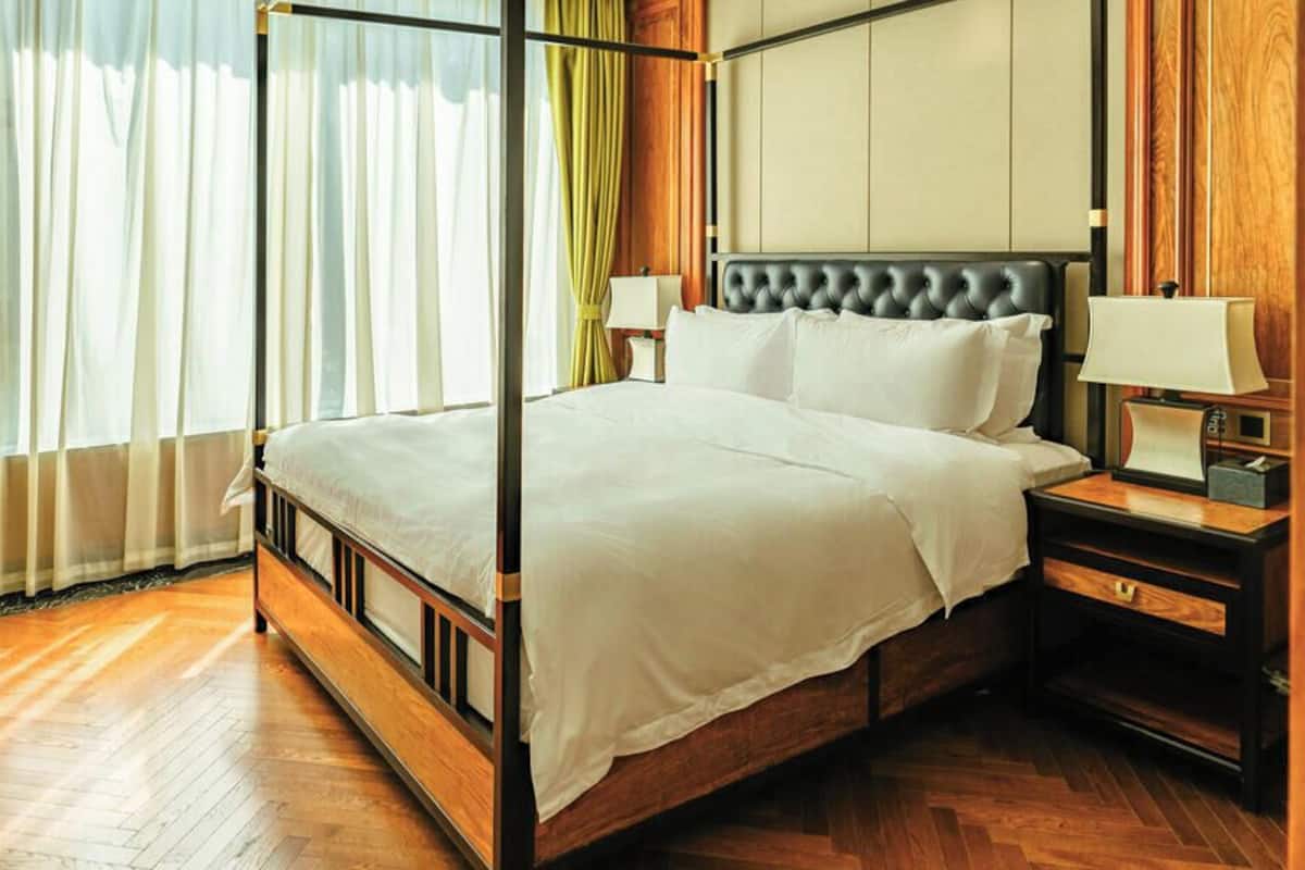 A four-poster bed with a wooden frame, a headboard with tufting, two bedside tables with lamps, and a wooden floor.