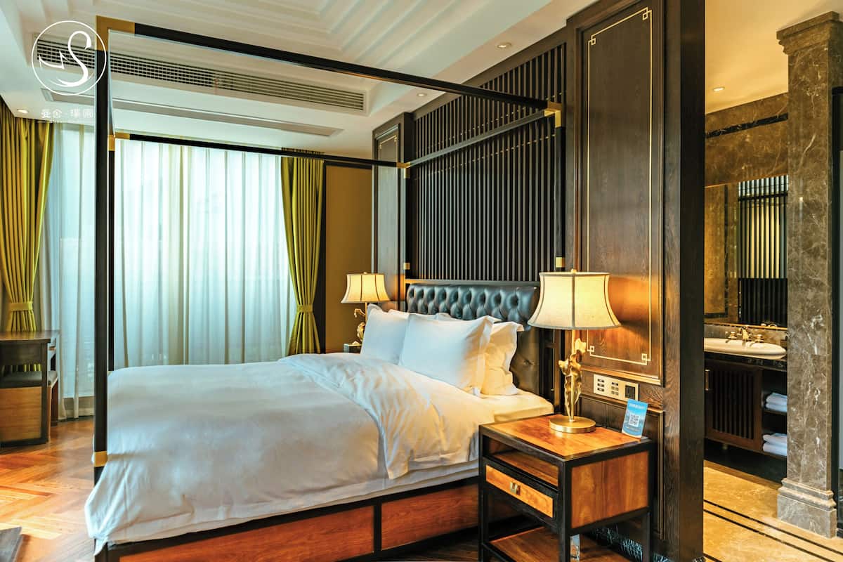 Ein Hotelzimmer mit einem großen Bett, Nachttischlampen, einem Nachttisch, einem Spiegel und einem Badezimmer mit Waschbecken und Spiegel.