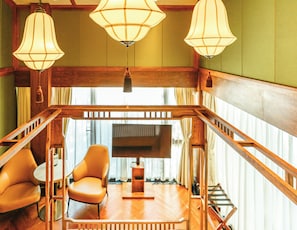 A room with a wooden staircase, two leather armchairs, a wooden coffee table, and three hanging lamps.