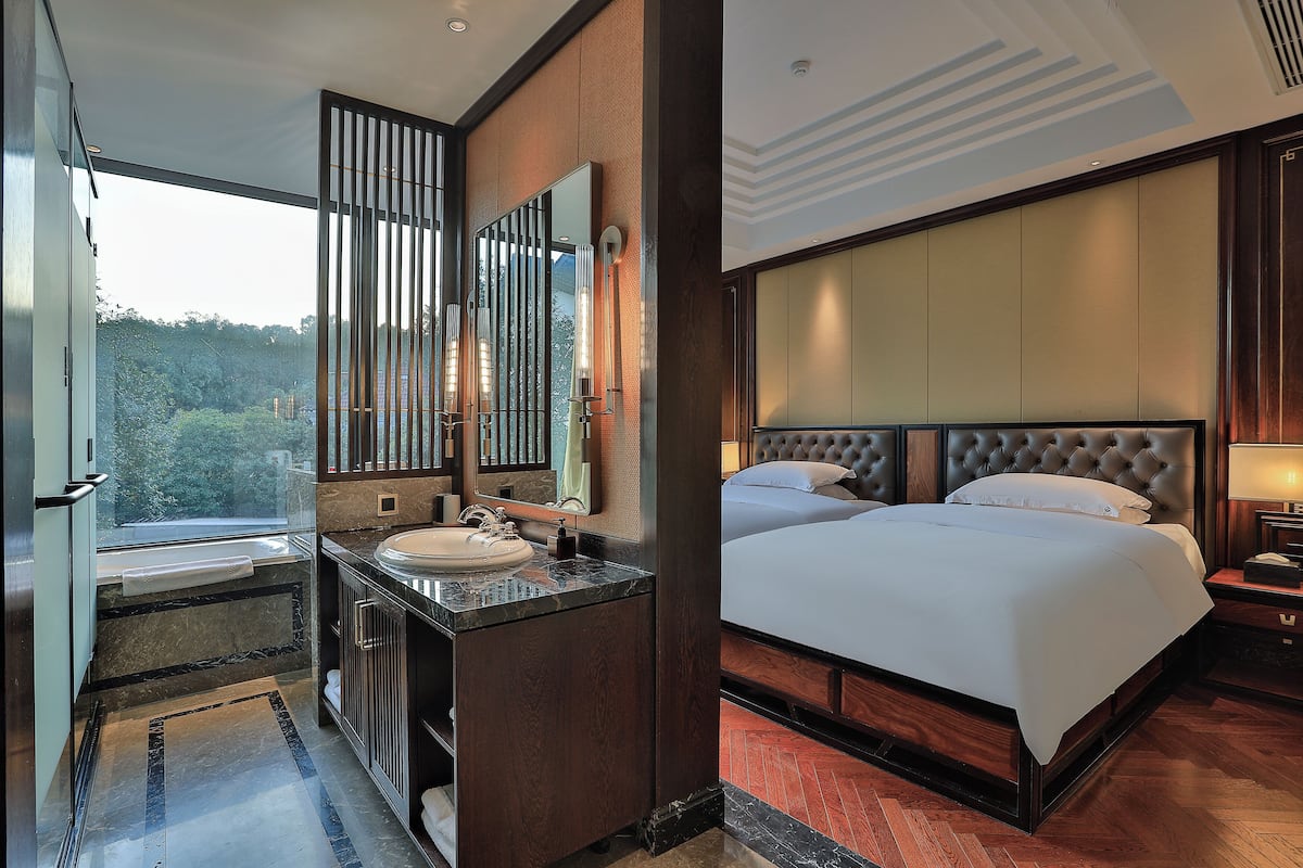 Ein modernes Hotelzimmer mit einem großen Bett, einem Badezimmer mit Waschbecken und Spiegel sowie Blick ins Freie.