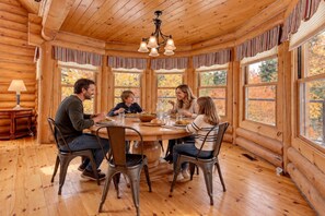 A wooden cabin interior with a round dining table, chairs, and a chandelier. - Lynx 72 | Private SPA | Heated Pool | GYM (Mille-Isles)