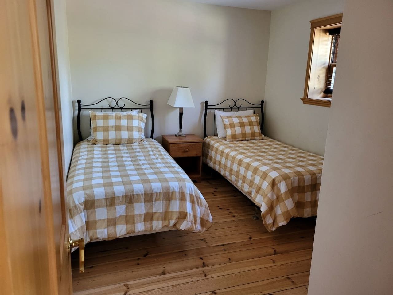 Une chambre avec deux lits, chacun recouvert d’une couvre-lit à carreaux, une table de chevet avec une lampe et une petite fenêtre.