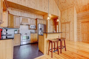 A wooden interior with a kitchen featuring a stove, oven, microwave, and refrigerator. There are wooden stools and a small bar area.