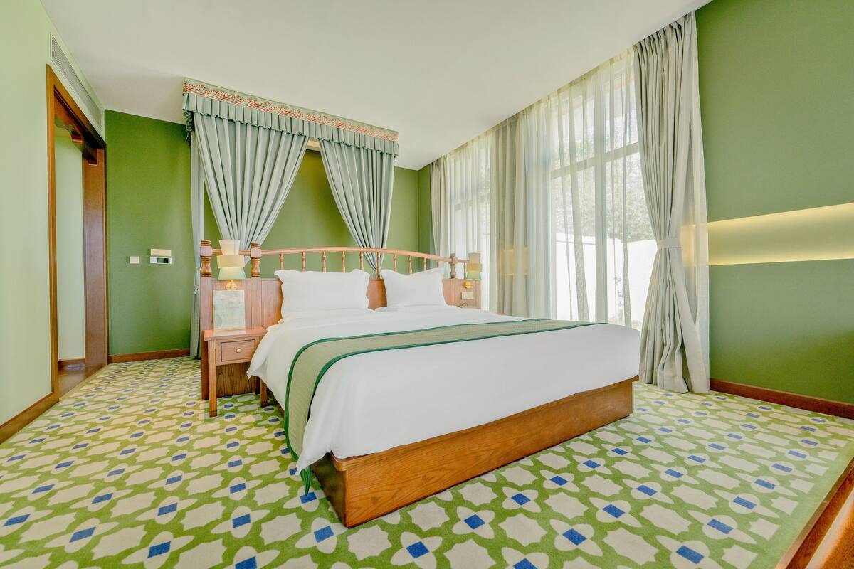 Una habitación de hotel con una cama grande, una mesita de noche y un ventanal con cortinas.