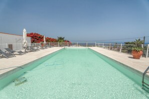 A rectangular swimming pool with clear water, surrounded by a white fence, and a view of the sea in the background.