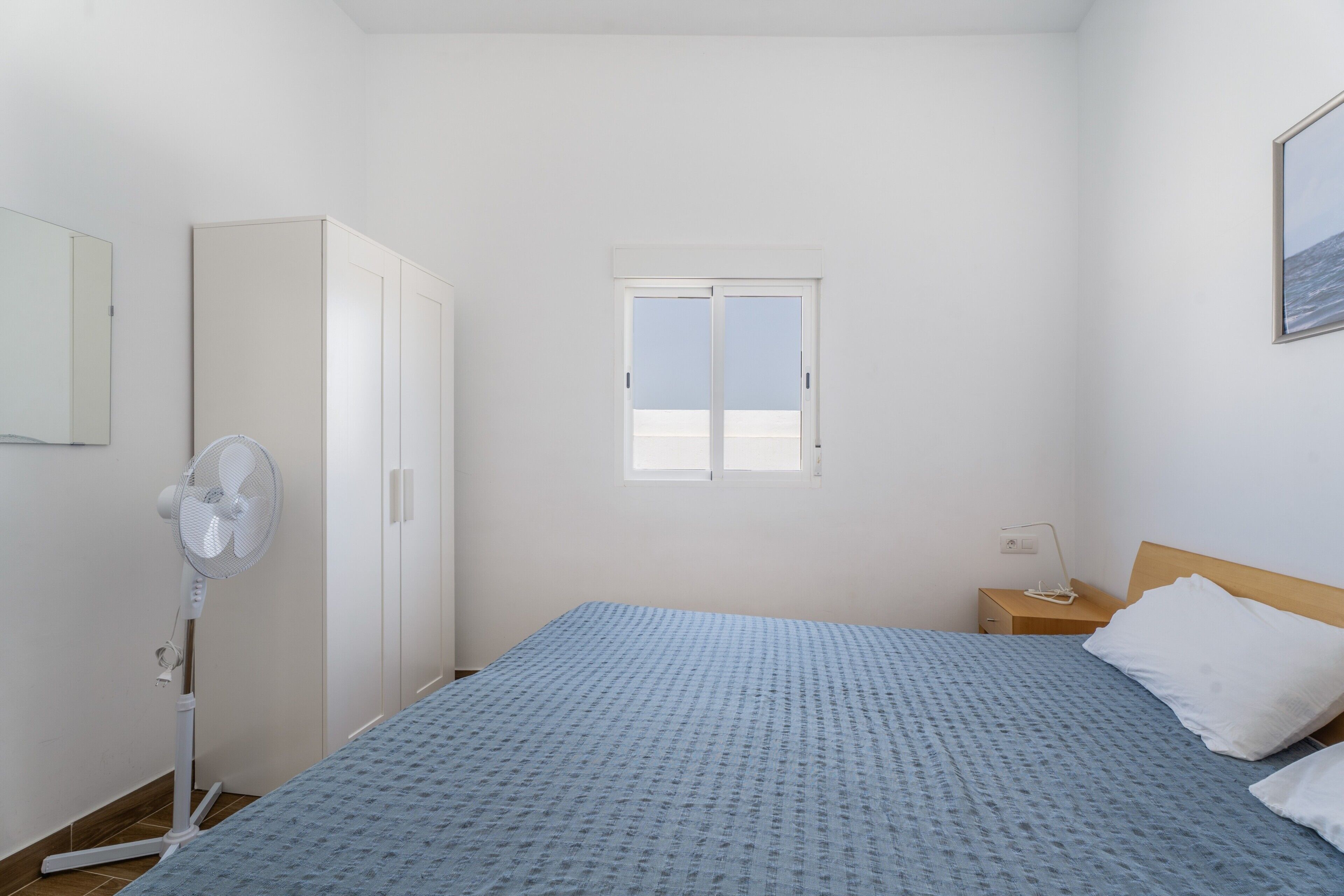 A bedroom with a bed, a wardrobe, a window, and a fan.
