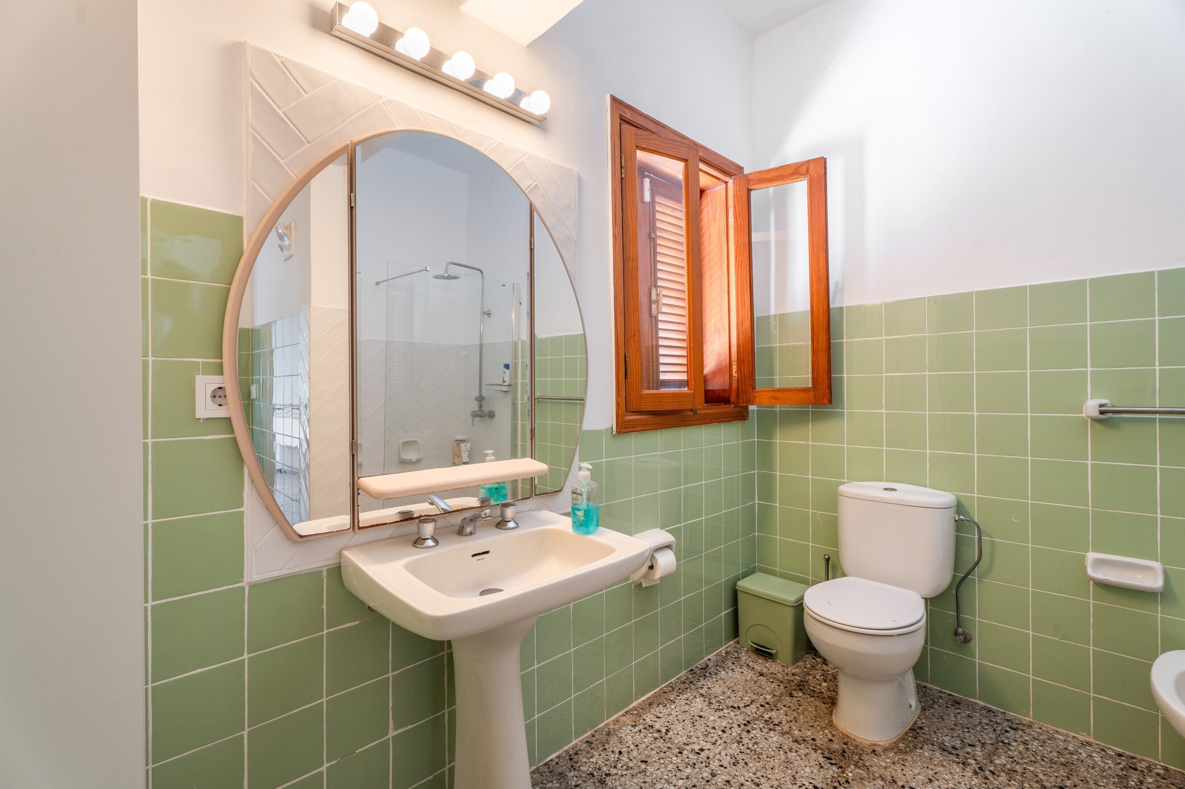 A bathroom with a sink, mirror, toilet, and a window with blinds.