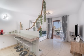 Uma cozinha moderna com área de bar, espaço de jantar com vista e uma TV sobre um armário de madeira.