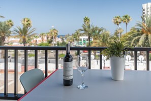 Uma varanda com uma mesa, uma garrafa de vinho Celeste, um copo e um vaso com planta.