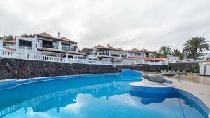 En swimmingpool med en stenvæg, hvide hegn og bygninger med tagsten.