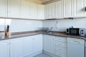 Una cocina con armarios blancos, encimera de granito, pileta, microondas y lavavajillas.