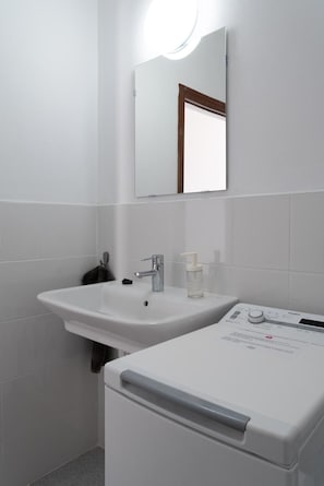 Un baño con un lavabo blanco, un espejo y una lavadora blanca.