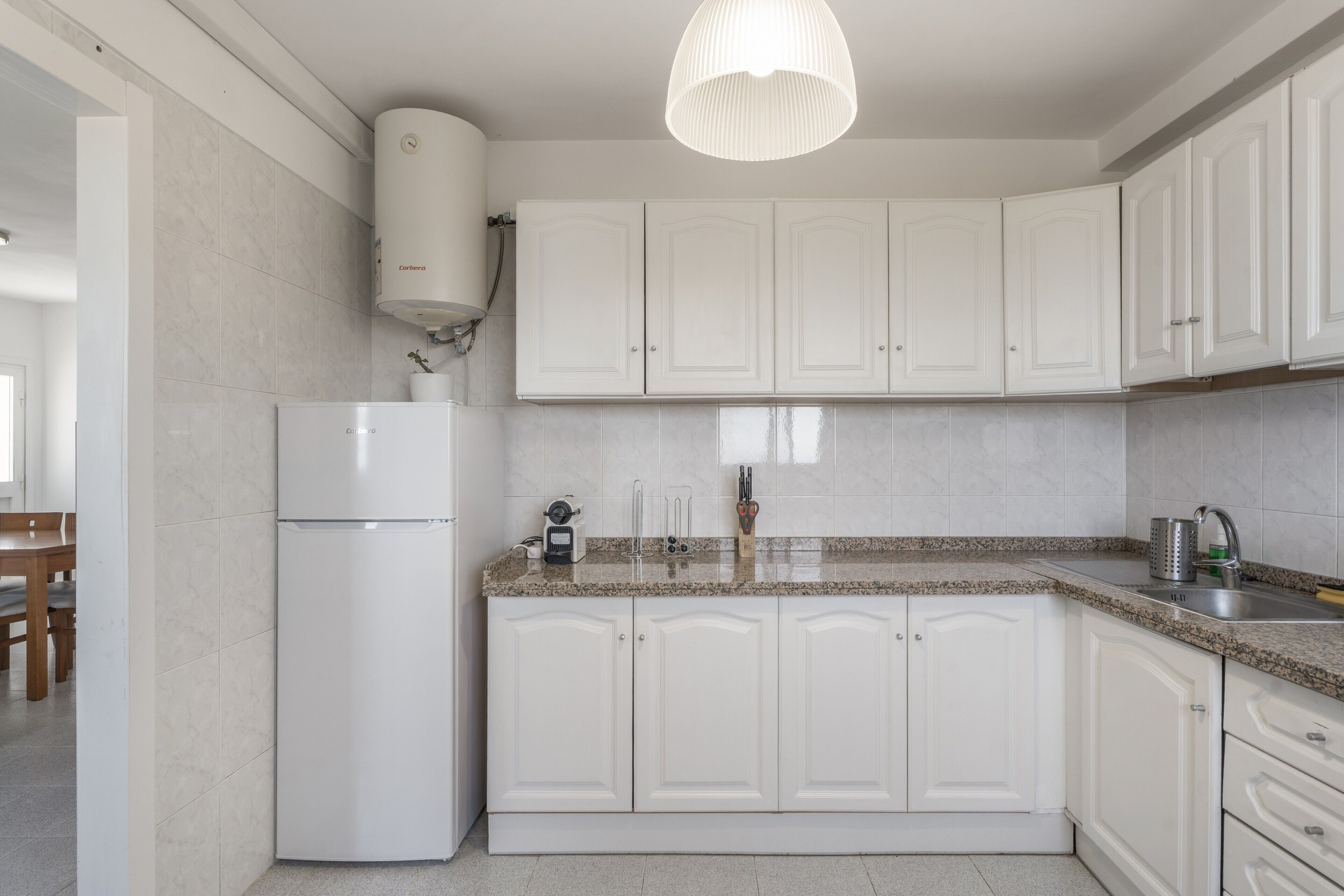 Una cocina moderna con armarios blancos, horno empotrado y encimera de granito.