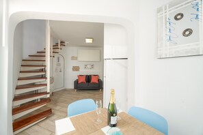 A modern interior with a staircase, a dining table with two chairs, a bottle of champagne, and a sofa in the background. - Holiday Apartment 'San Rafael' with Sea View, Shared Pool and Wi-Fi (Playa de las Américas)