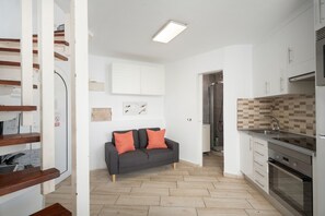 A modern kitchen with white cabinets, a grey sofa with orange cushions, and a herringbone-patterned backsplash. - Holiday Apartment 'San Rafael' with Sea View, Shared Pool and Wi-Fi (Playa de las Américas)