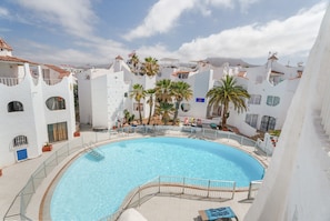 Une piscine entourée de bâtiments blancs dotés de balcons, de palmiers et surplombant un ciel dégagé.