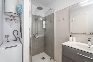 Ein modernes Badezimmer mit einer gläsernen Duschkabine, einem weißen Waschbecken mit Spiegel und einem Handtuchhalter.