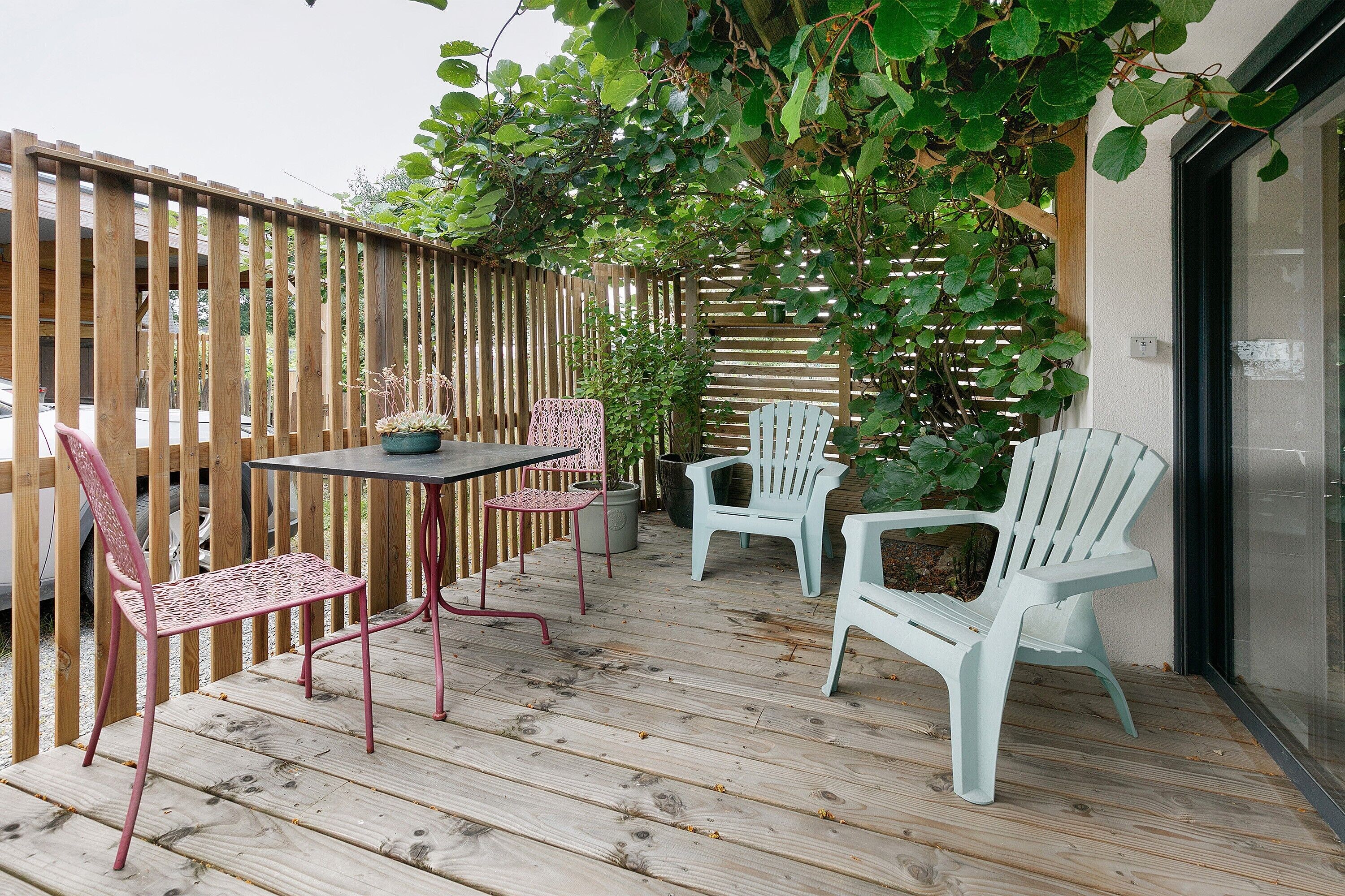 Una terraza de madera con una mesa y sillas, rodeada por una valla de madera y vegetación.
