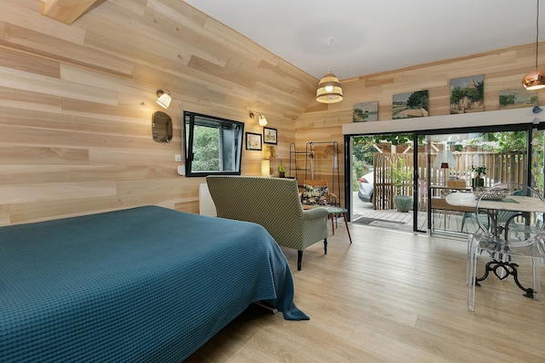 A room with a bed, a chair, a table, and a view of the outdoors.