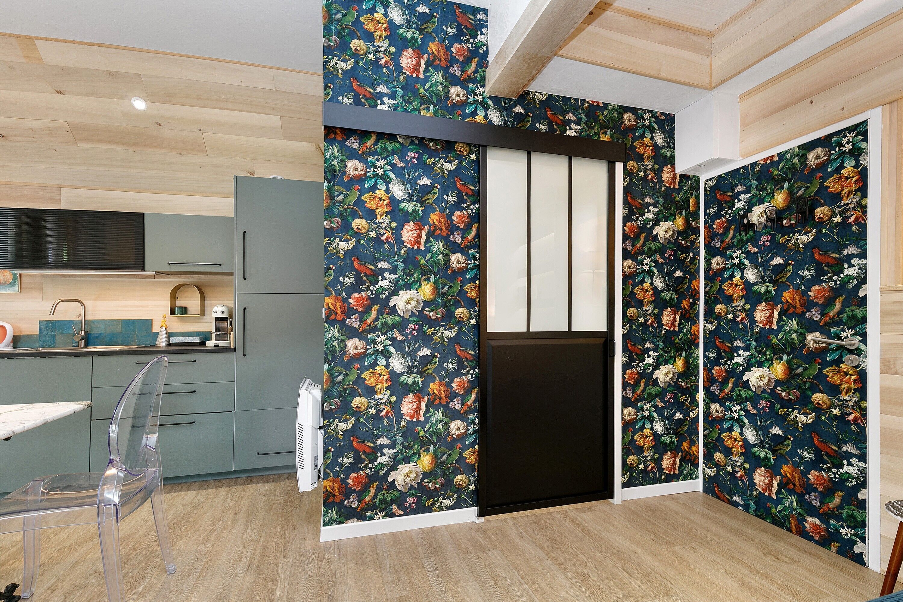 Une cuisine moderne avec des meubles gris, un plafond en bois et un papier peint à motifs floraux.