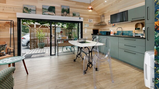 A modern kitchen with wooden flooring, a dining area with a table and chairs, and a view through a glass door to an outdoor patio. - Maison “Gîte Mimosas” with Terrace and Wi-Fi (Marzan)