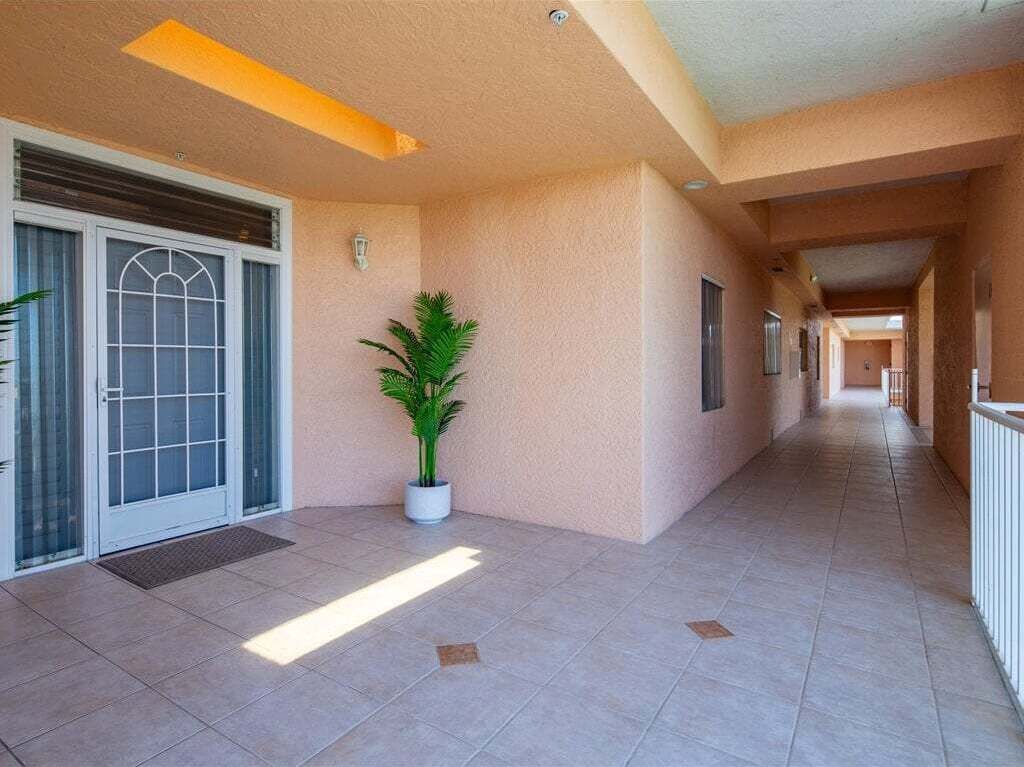 A corridor with a potted plant, a door with a window, and a tiled floor.
