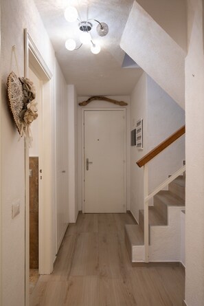 Ein Flur mit einer weißen Tür, einer Holztreppe und einer Deckenleuchte.