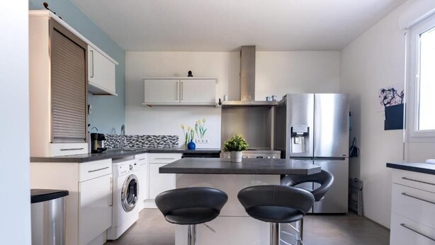 Cocina moderna con lavadora, dos taburetes, refrigerador y una ventana.