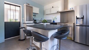 Una cocina moderna con una isla central, taburetes de bar, electrodomésticos de acero inoxidable y una ventana con persianas.