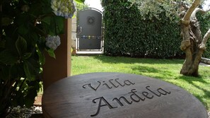 Ein Holzschild mit dem Namen 'Villa Andela' in einem Garten.