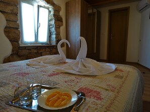 Ein Bett mit einer Schwan-Handtuch-Arrangement, Obstteller und Tablett mit Gläsern und Besteck.