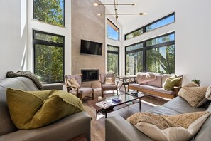 Ein modernes Wohnzimmer mit großen Fenstern, einem Flachbildfernseher und einem Kamin.