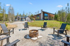 Eine moderne Holzhütte mit Steinaußenwand, einem Feuerkorb und Adirondack-Stühlen sowie einer Rasenfläche.