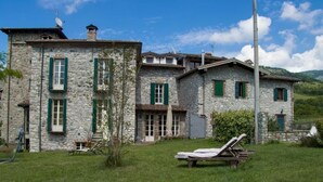 Un edificio in pietra con diverse finestre e un'entrata, circondato da un'area verde con una sedia a sdraio.